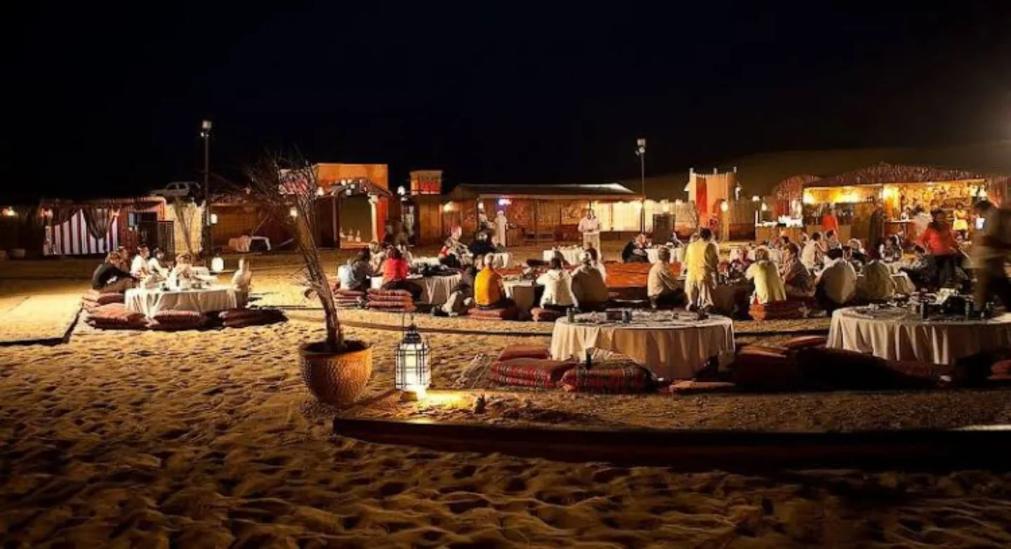 Guests seated for an evening meal at a lit desert camp